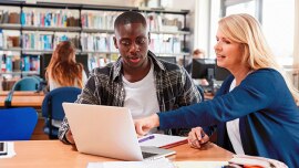 a woman pointing at a laptop while explaining something to a student