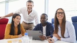 People it at table, in front of a laptop, smiling at the camera